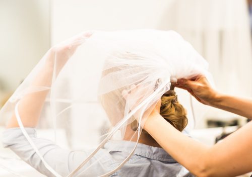 Stylist pinning up a bride's hairstyle and bridal veil before the wedding